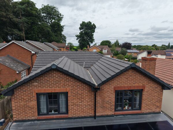Exterior aerial view of a modern brick property, showing the roofline, frontage and surrounding homes.
